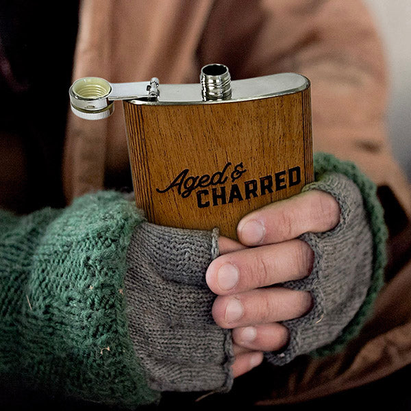 A person holding 6oz stainless steel flask wrapped in real mahogany wood; Includes funnel and leak-proof cap