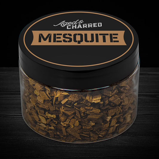 A clear container filled with mesquite wood chips, intended for whiskey infusion.