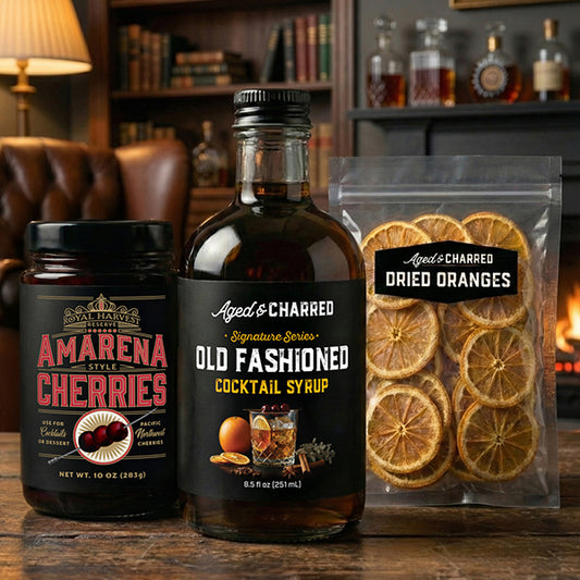 Bottles of Aged & Charred Amarena Style Cherries and Old Fashioned Cocktail Syrup, with a package of dried oranges on a wooden surface.
