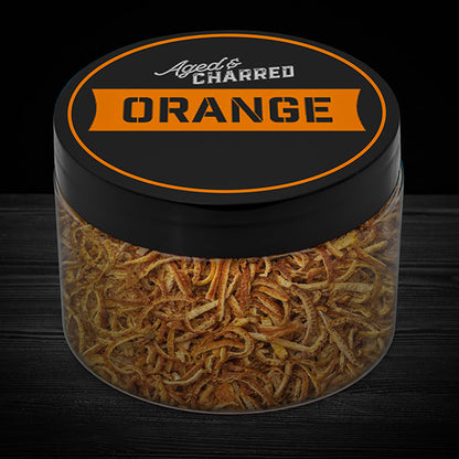 A clear container filled with aged and charred orange peel, with a black lid featuring the text 'AGED CHARRED ORANGE' on it.