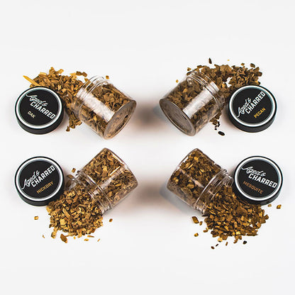 Four containers labeled Aged & Charred with different types of wood chips spilled: pecan, mesquite, hickory, and oak